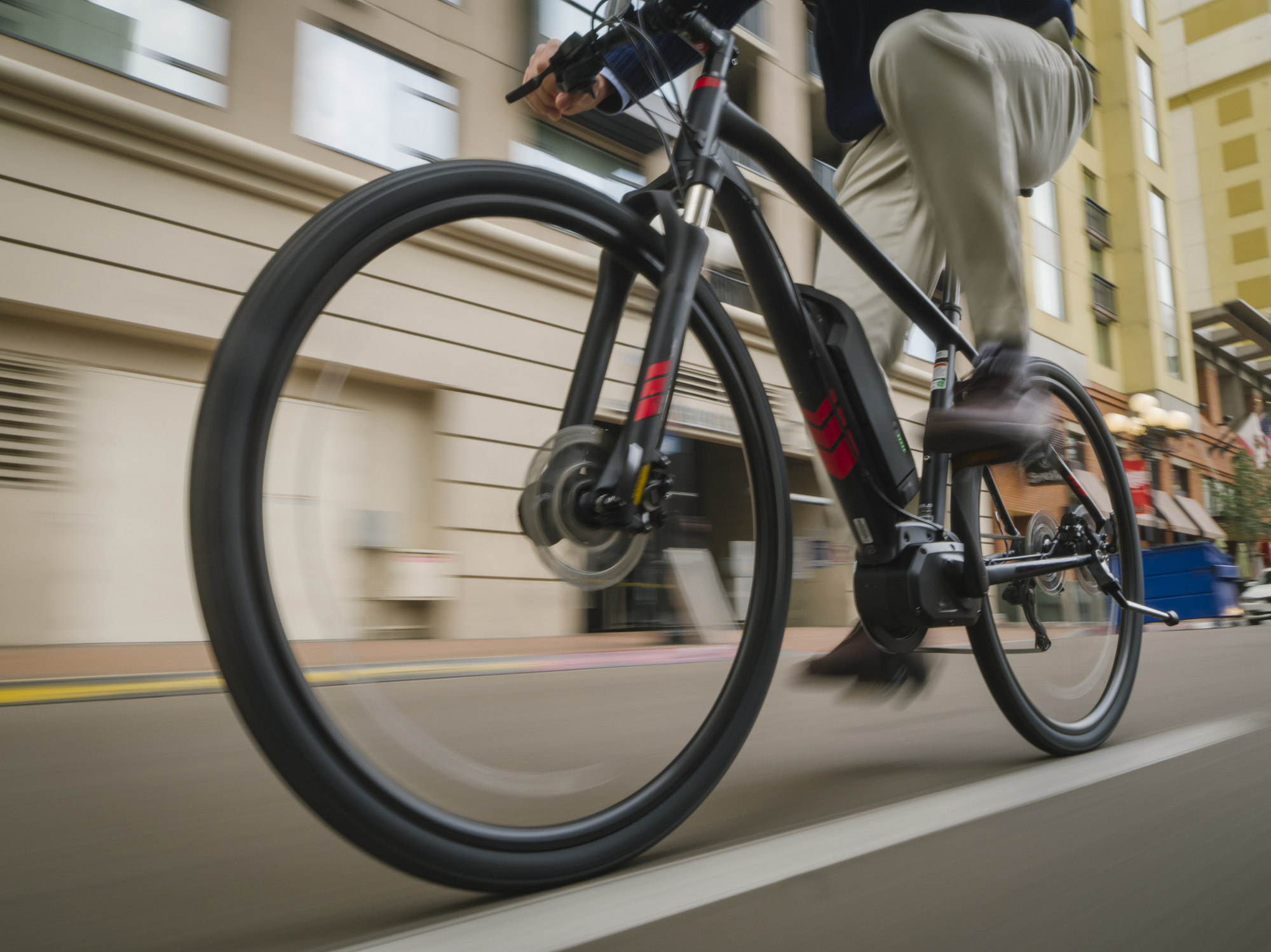 a professional businessman commutes to work on his electric battery powered ebike wearing casual business clothing and a helmet and backpack along a bike lane through the car traffic filled streets of San Diego, California, USA