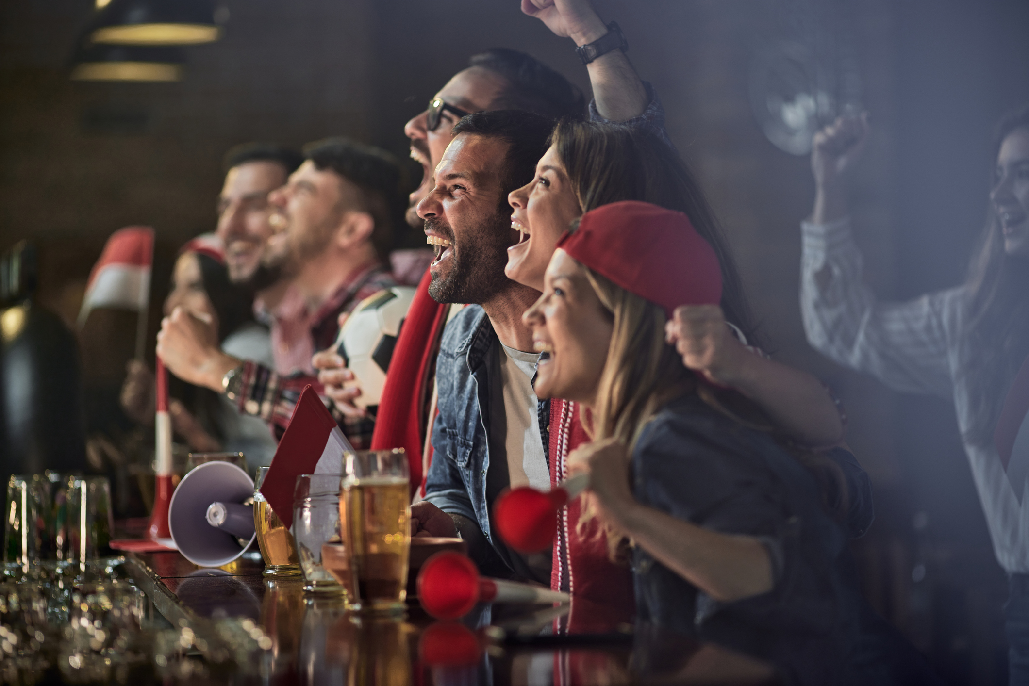 Large group of cheerful soccer fans screaming while celebrating the victory of their favorite team in a pub.